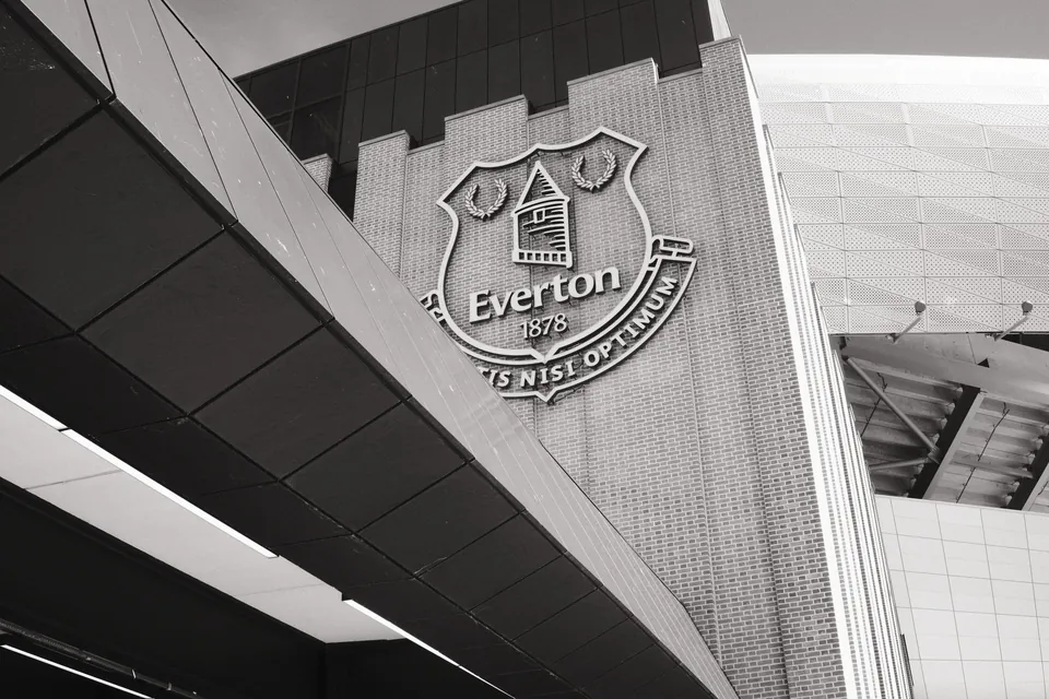 An angled black-and-white view of the Everton crest on the brick exterior of Bramley Moore (Hill Dickinson Stadium).