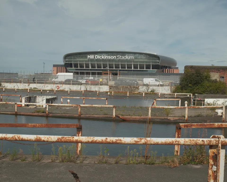 Photograph: Hill Dickinson Stadium beyond dock water and weathered railings.